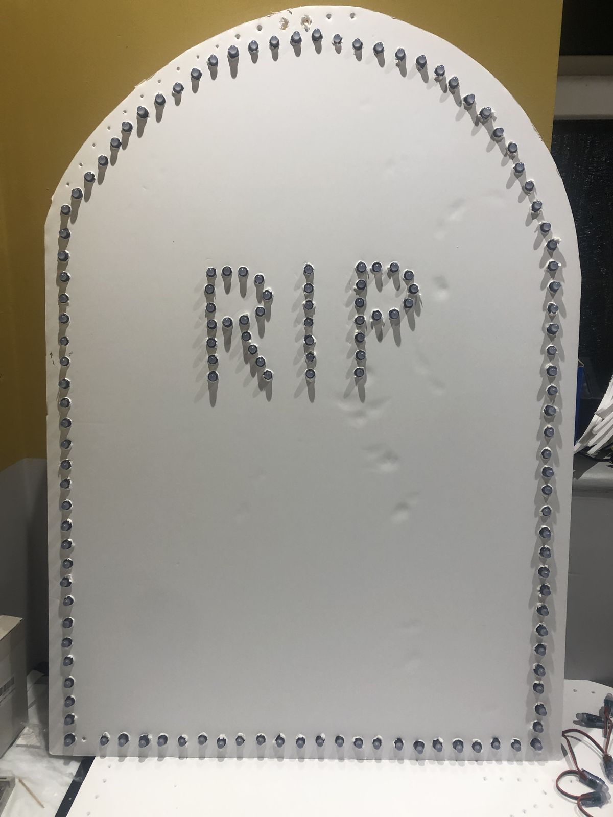 A white foam board tombstone outlined in pixels, with RIP spelled out in the middle